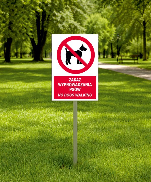 Tabliczka dwujęzyczna na słupku z piktogramem psa na smyczy i napisem po polsku i angielsku „Zakaz wyprowadzania psów / No dogs walking”.